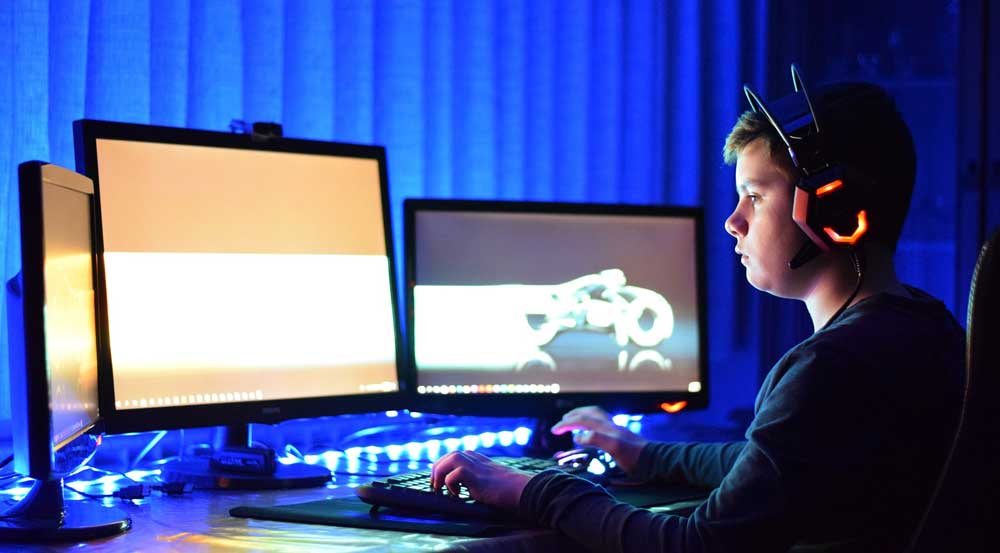 Jugendlicher spielt am PC mit Headset und mehreren Monitoren